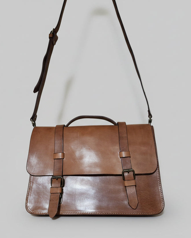 Brown leather bag with straps on a wooden surface