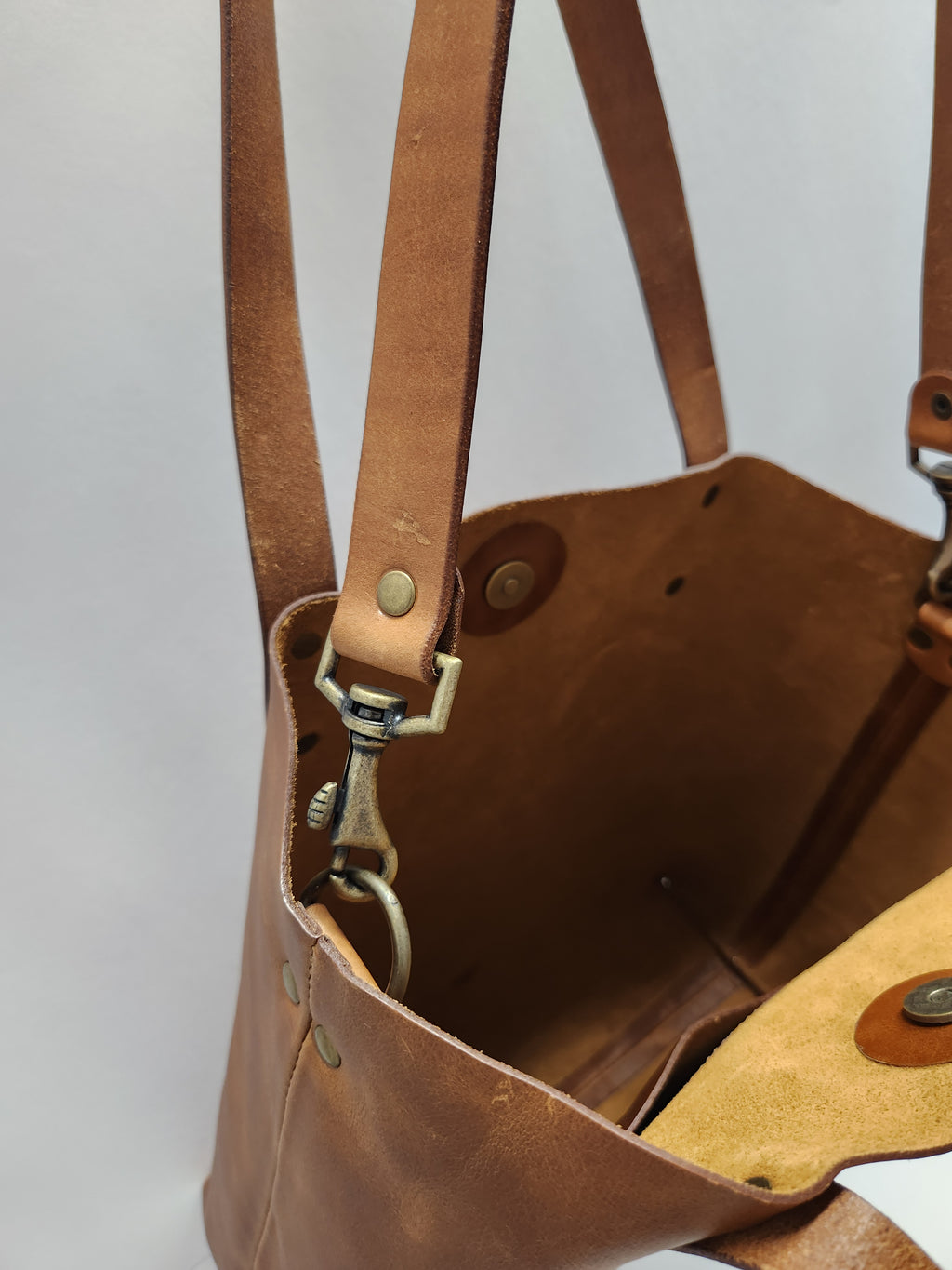 Close-up of a brown leather bag with visible stitching and hardware on a light gray background