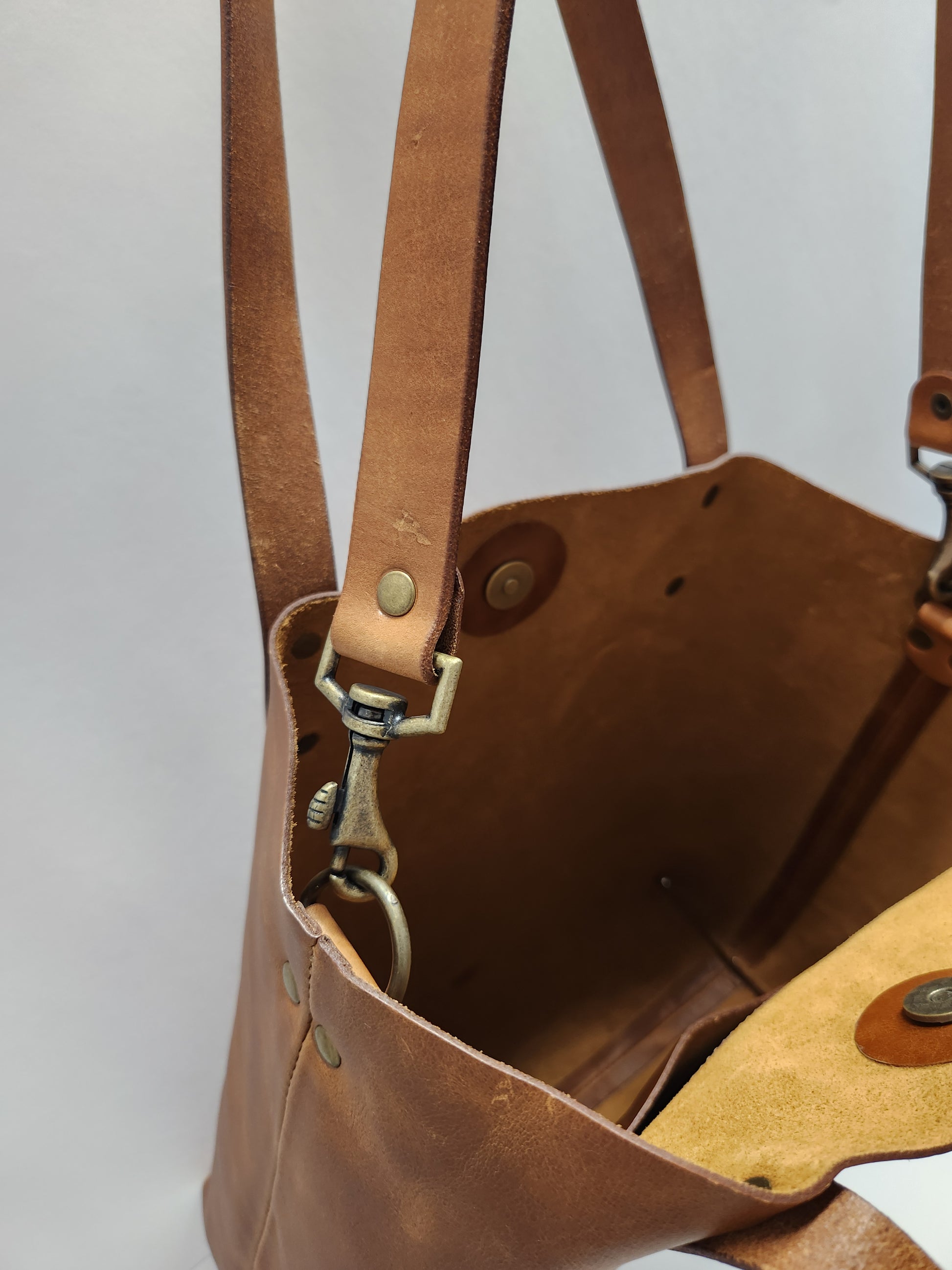 Close-up of a brown leather bag with visible stitching and hardware on a light gray background