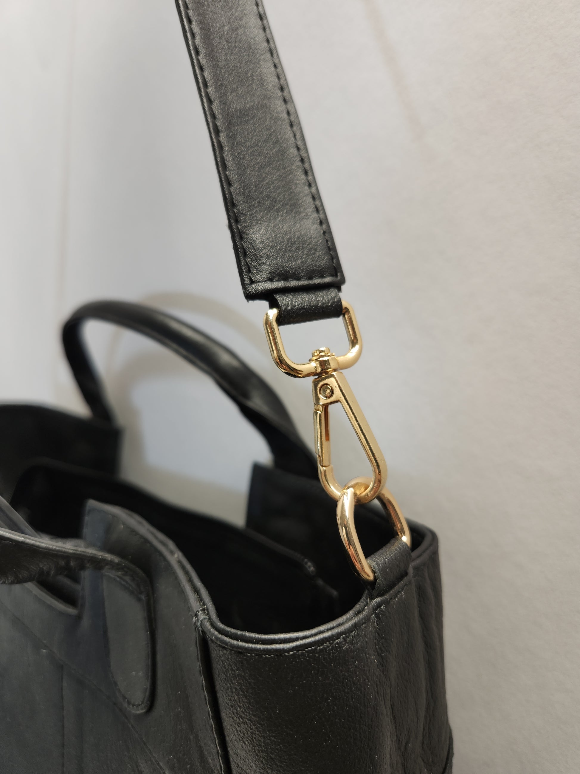 Black handbag with a gold clasp on a light gray background