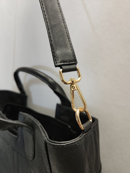 Black handbag with a gold clasp on a light gray background