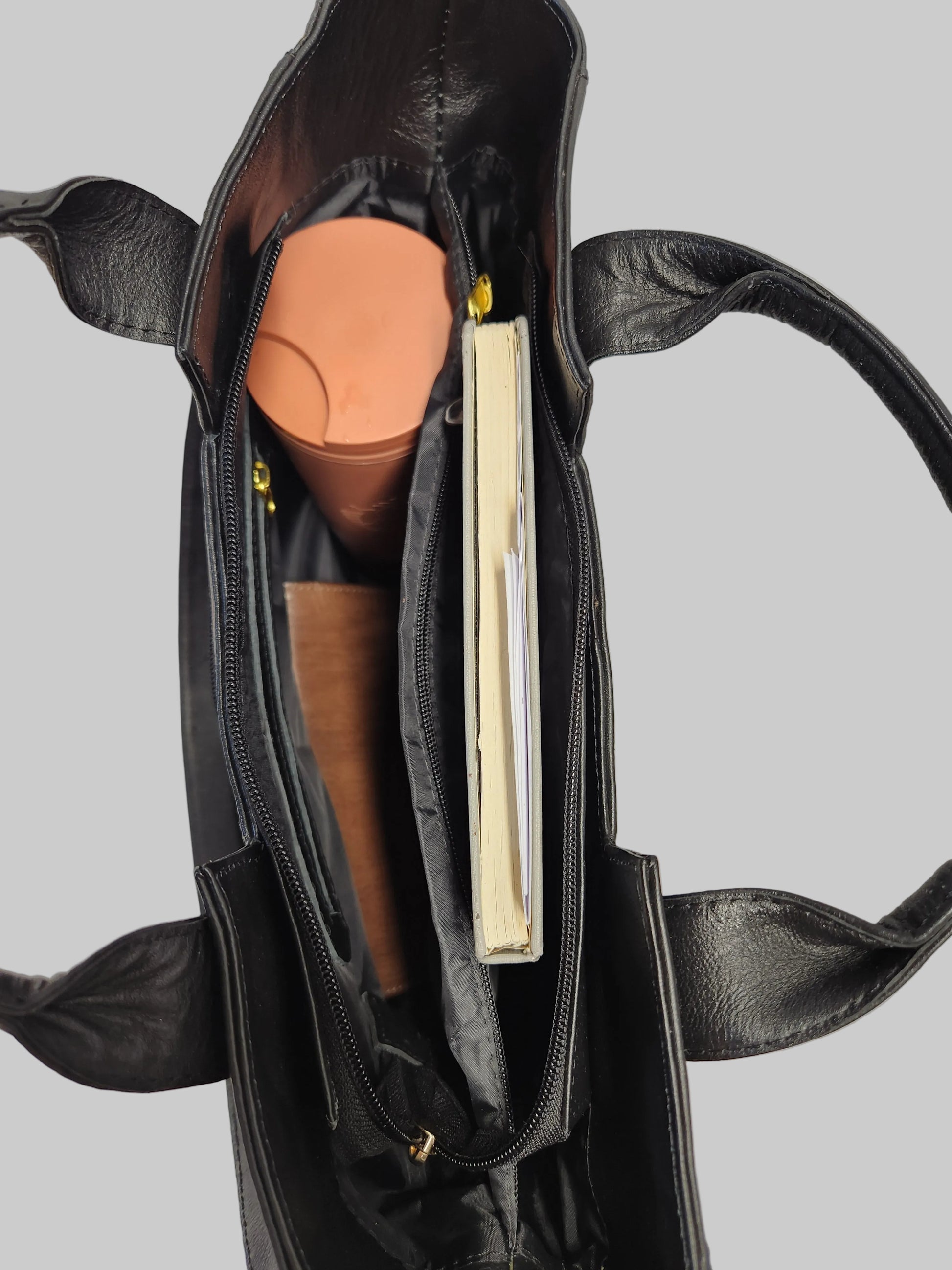 Black leather handbag with a book and cylindrical object inside on a light gray background