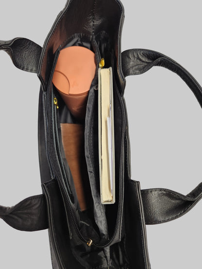 Black leather handbag with a book and cylindrical object inside on a light gray background