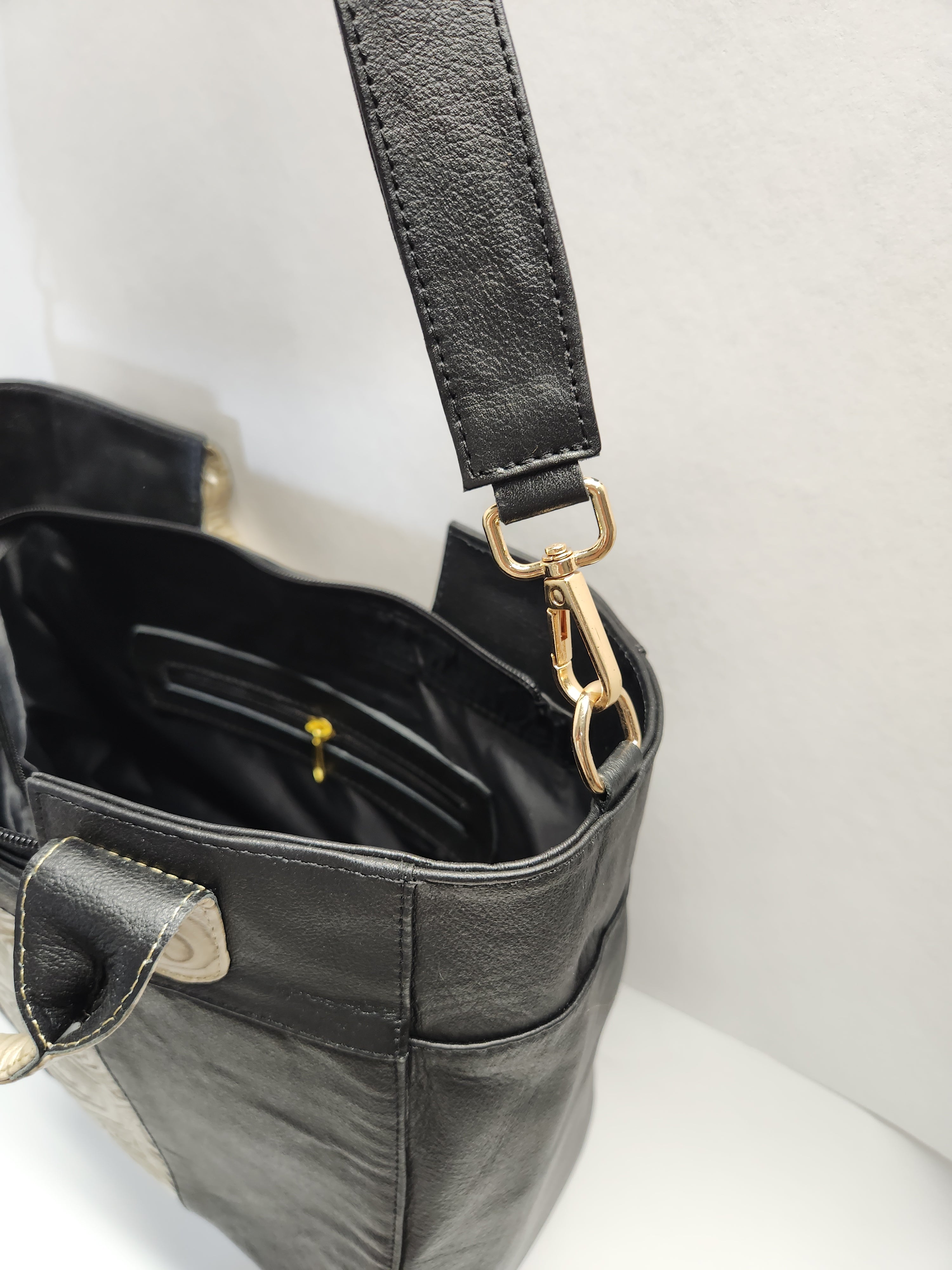 Black leather handbag with gold clasp on a light gray background