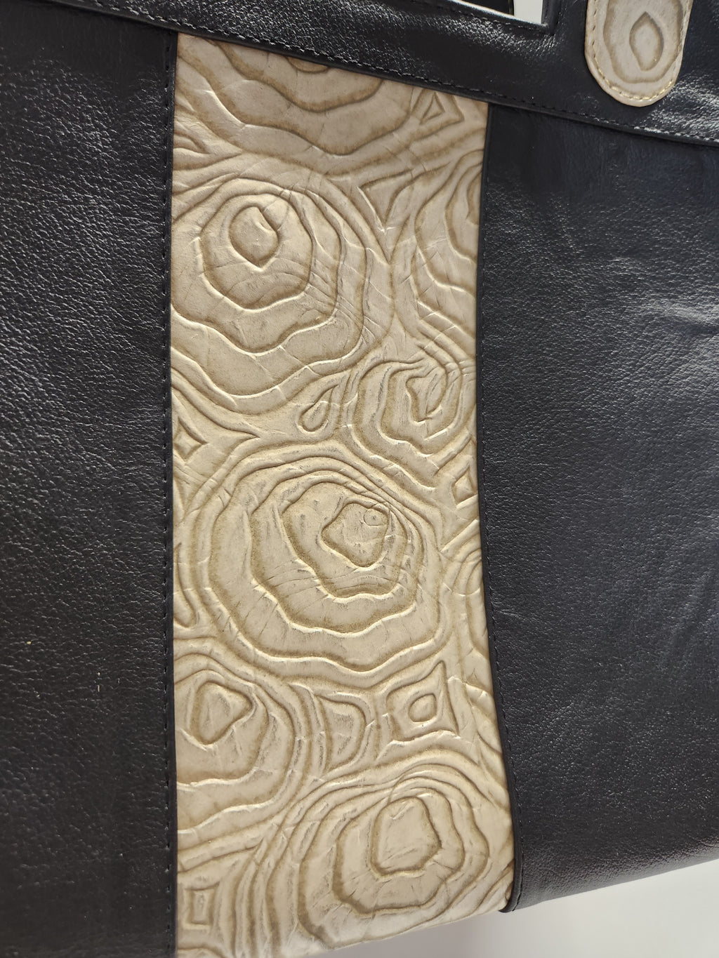 Close-up of a black leather bag with beige embossed design
