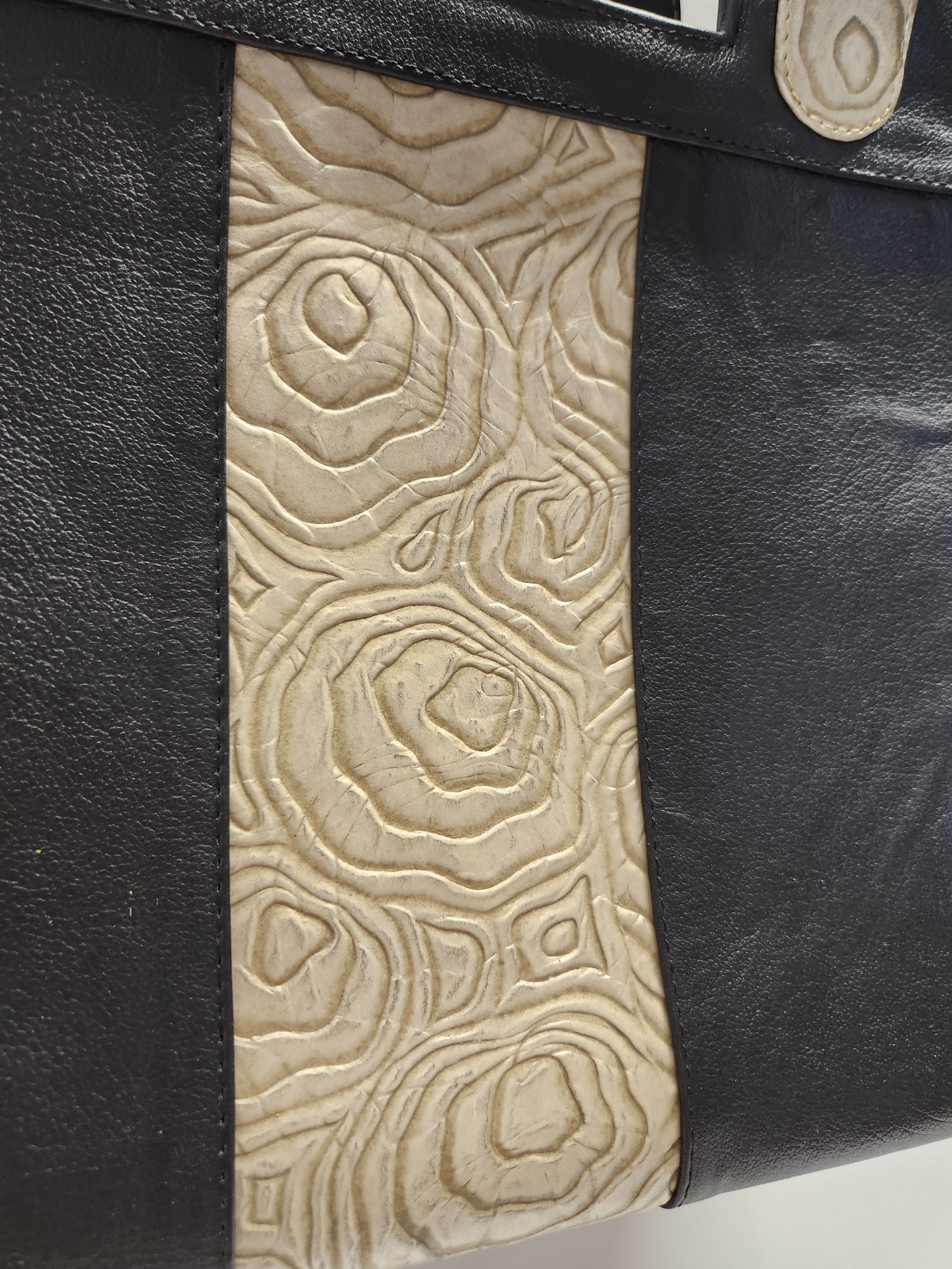 Close-up of a black leather bag with beige embossed design