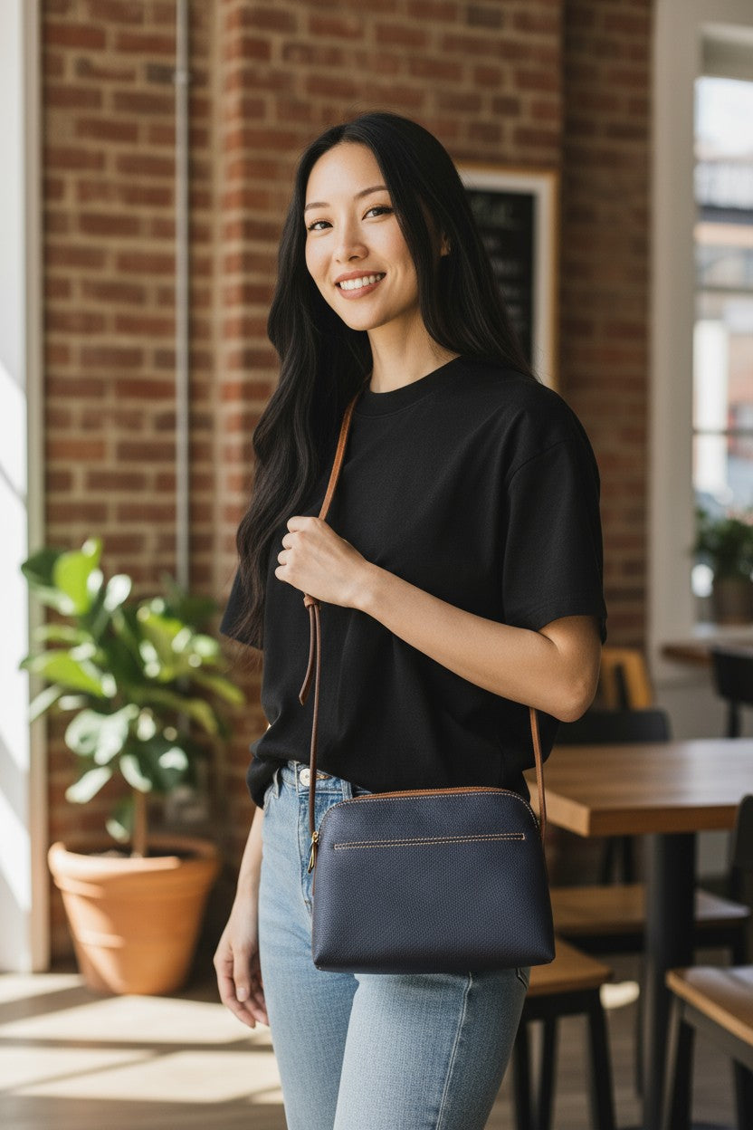 Woman holding a navy blue handbag in an indoor setting with brick walls and plants.