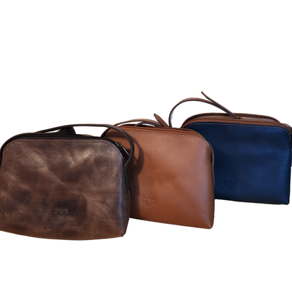 Three leather bags in brown, tan, and blue on a wooden surface with a wooden panel background.