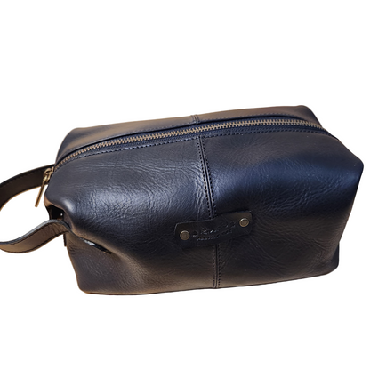 Black leather toiletry bag with a handle on a wooden surface
