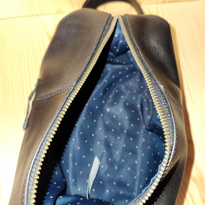 Brown leather bag with blue interior lining on a beige surface