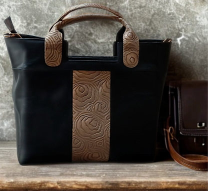 Black handbag with brown leather strap and decorative handle on a wooden surface.