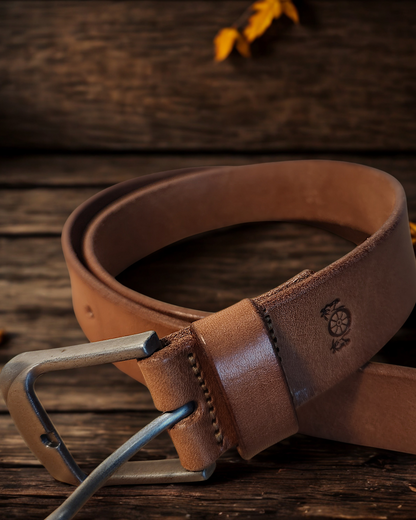 Brown leather belt with a silver buckle on a wooden surface with autumn leaves.