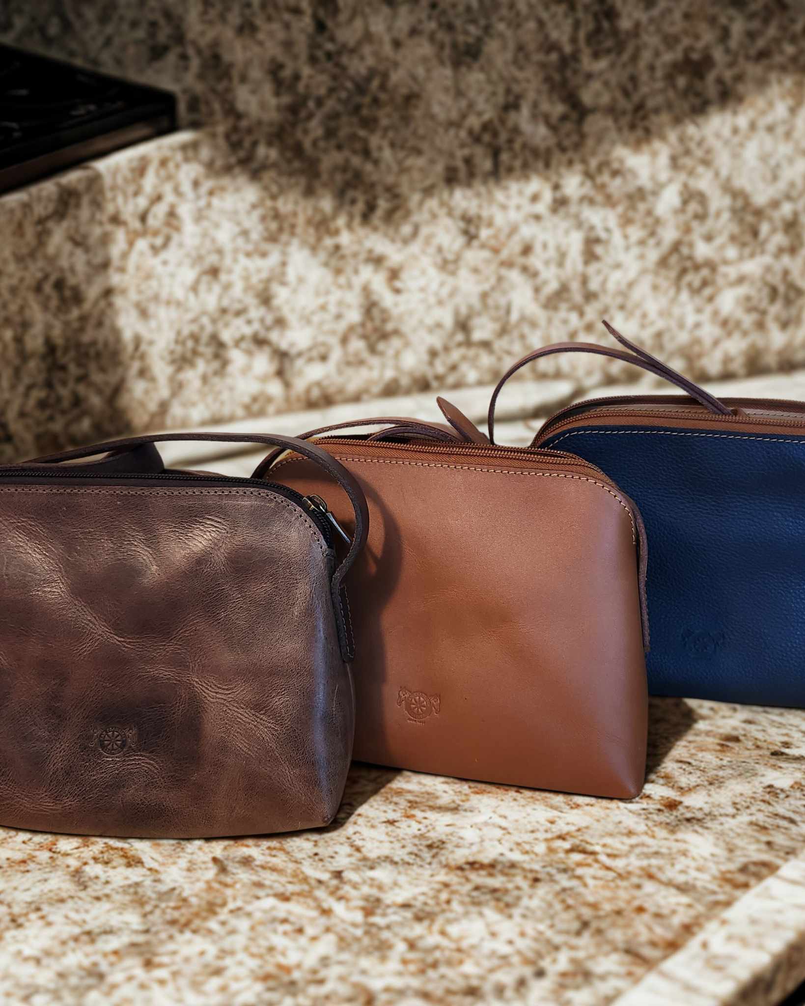 Three leather bags in brown, tan, and blue on a stone surface.