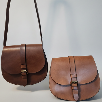 Two brown leather bags on a wooden surface with autumn leaves.
