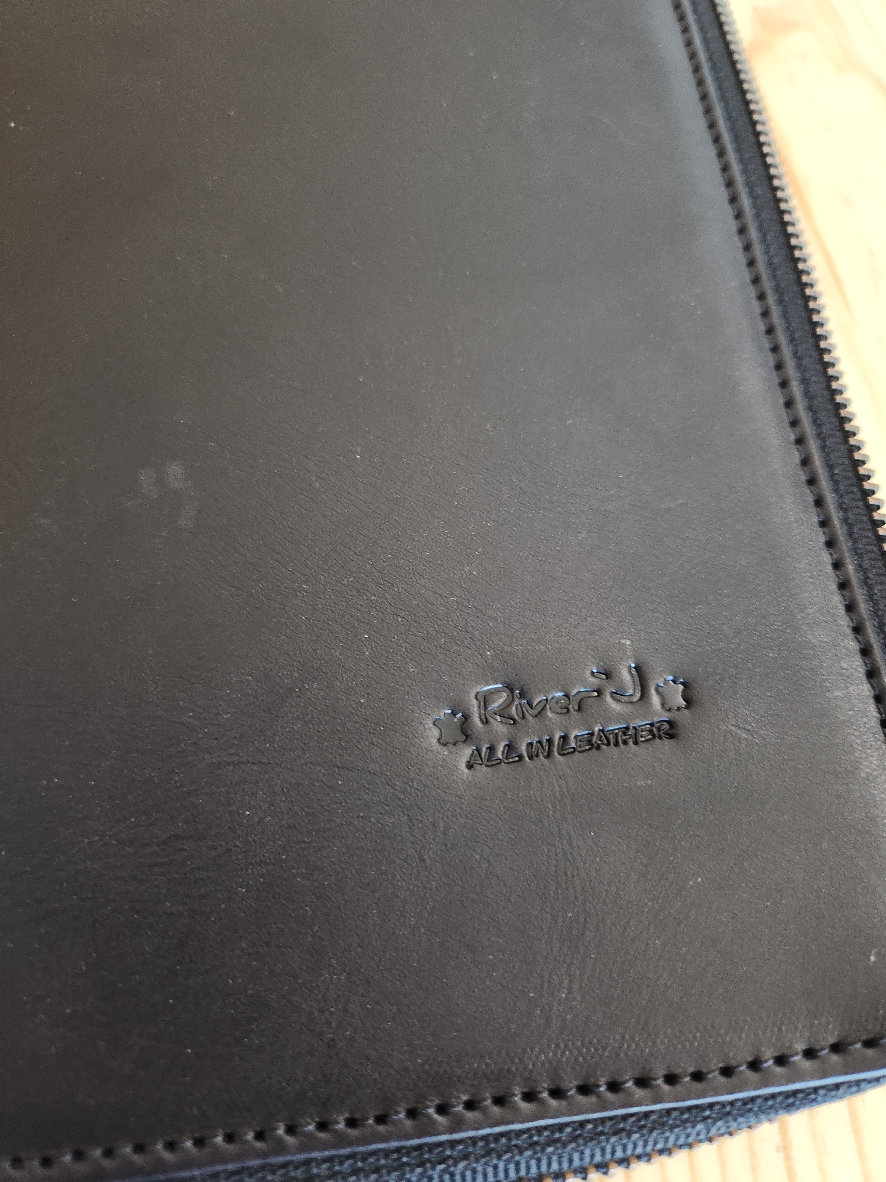Close-up of a black leather product with a brand logo on a wooden surface