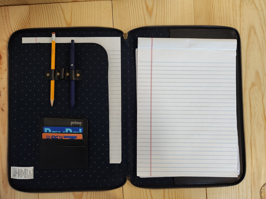 Black zippered pouch with a pen, notebook, and card holder on a wooden surface