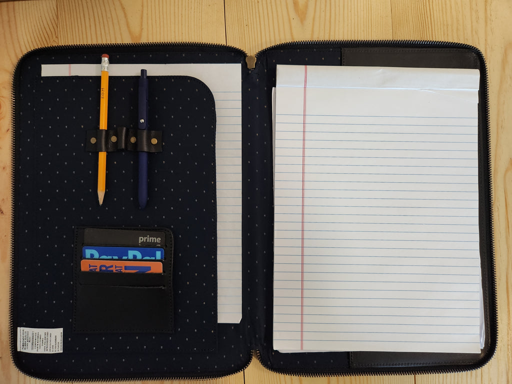 Open notebook case with writing utensils and lined paper on a wooden surface